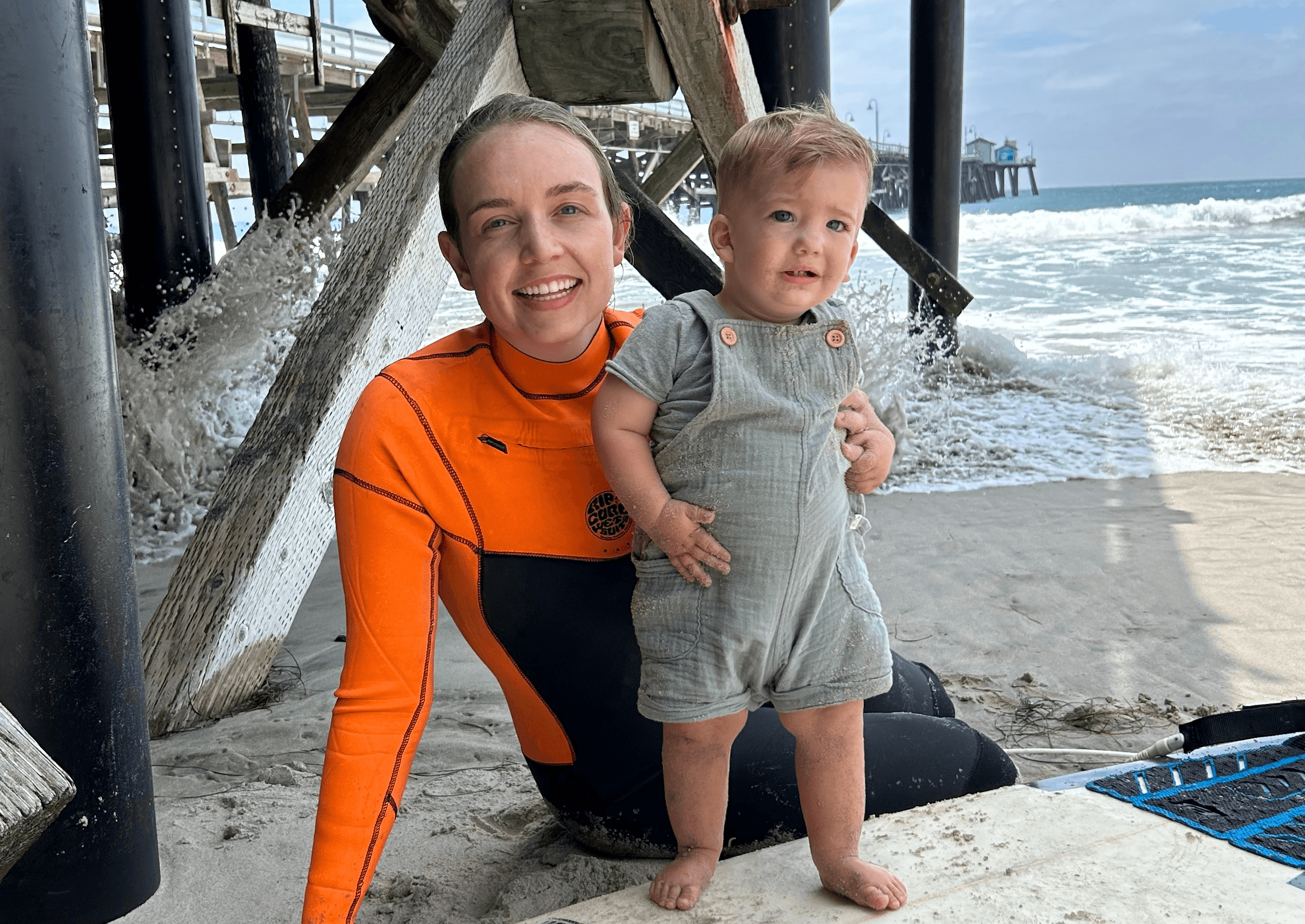 mom and baby at the beach with a surfboard